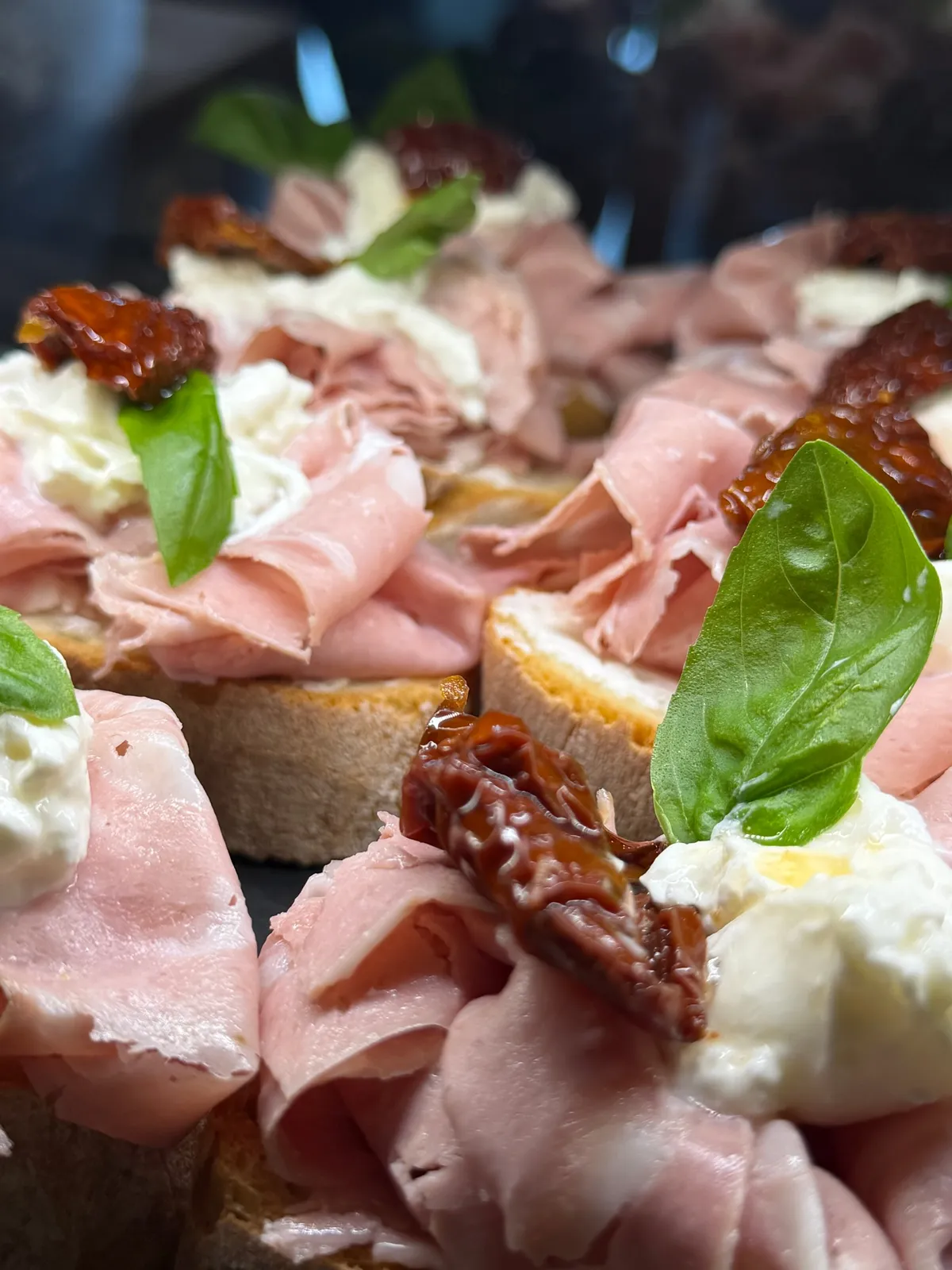 Crostini di mortadella con burrata, pomodori secchi e basilico